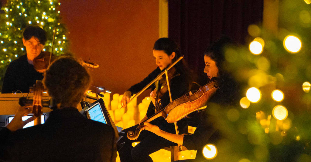 Des musiciens jouent entourés de bougies et de sapins de Noël lors du concert de Noël aux chandelles.