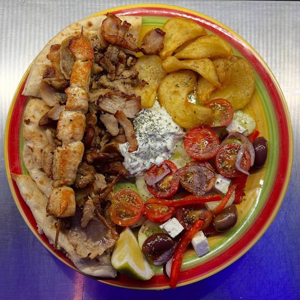 Assiette mixte avec gyros de porc, souvlaki de poulet, frites, salade grecque, sauce tzatziki et pita grecque.