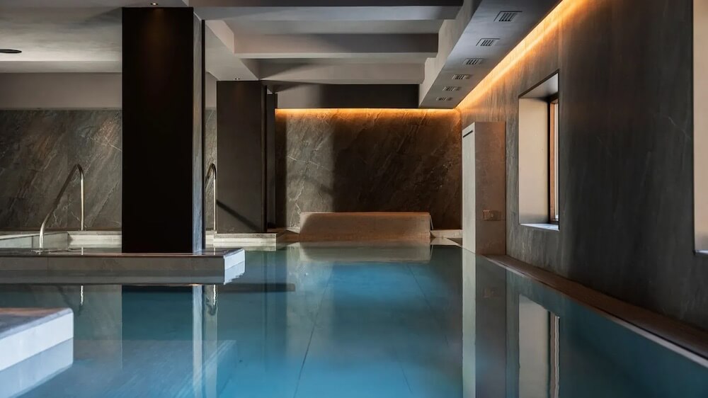 An elegant indoor pool with azure water, surrounded by dark stone walls and illuminated by soft LED lighting.