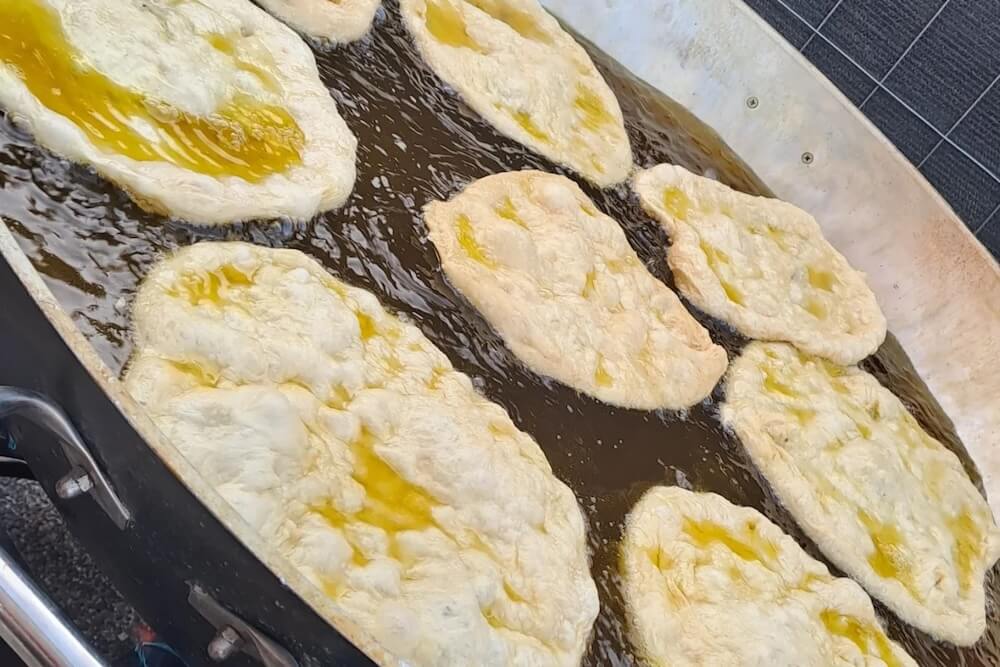 Verschiedene goldbraune, unregelmäßig geformte frittierte Pizzen, die in einer großen Pfanne voller heißem Öl brutzeln.