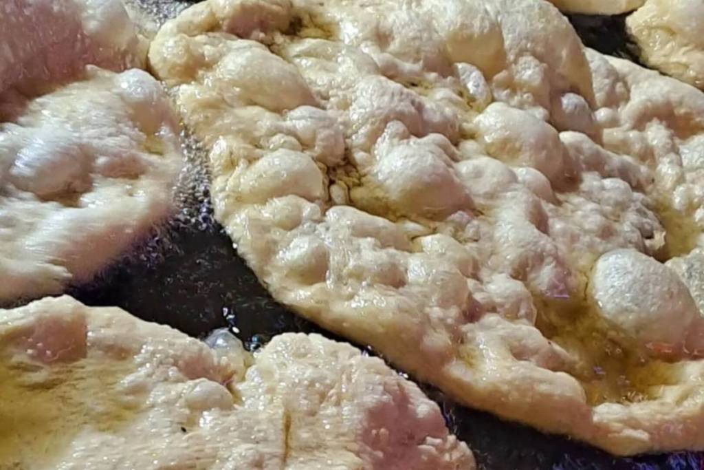 Nahaufnahme von unregelmäßigen, aufgeblähten frittierten Pizzen, die in reichlich heißem Öl gebacken werden und eine goldbraune, knusprige Oberfläche zeigen.