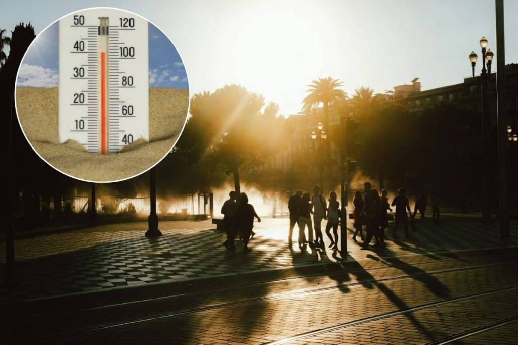 Un termometro a mercurio con temperatura di 40 gradi Celsius, con persone che passeggiano in una piazza durante l'ora d'oro al tramonto, con palme e illuminazione urbana sullo sfondo.