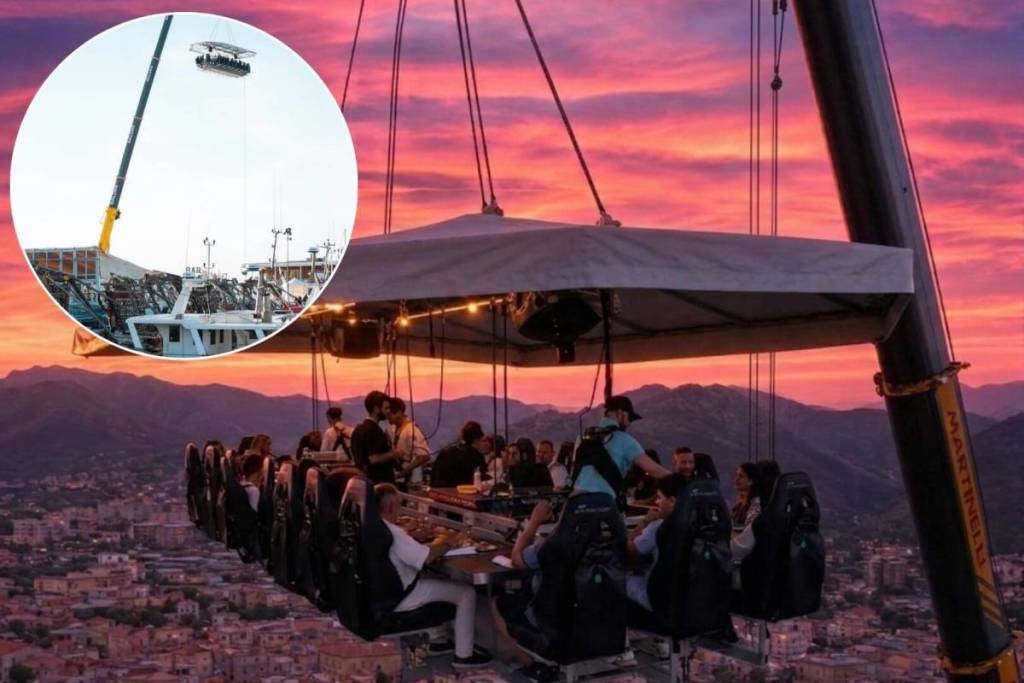Persone sedute a un tavolo sospeso nel vuoto durante un'esperienza di Dinner in the Sky al tramonto, con vista panoramica sulla città e sulle montagne.