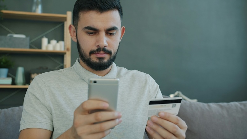 Persona che utilizza uno smartphone e una carta di credito per effettuare un acquisto online.