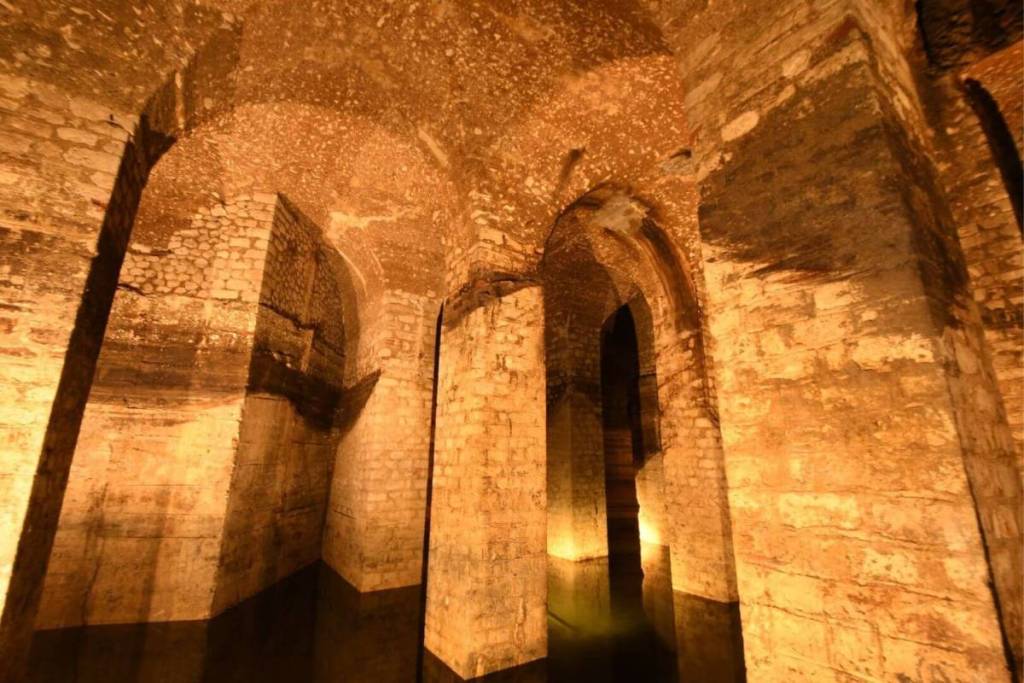 Interno del Cisternone Romano di Formia con pilastri storici illuminati da luci calde che si riflettono sull'acqua sotterranea, meta ideale per gite fuori porta vicino Roma.