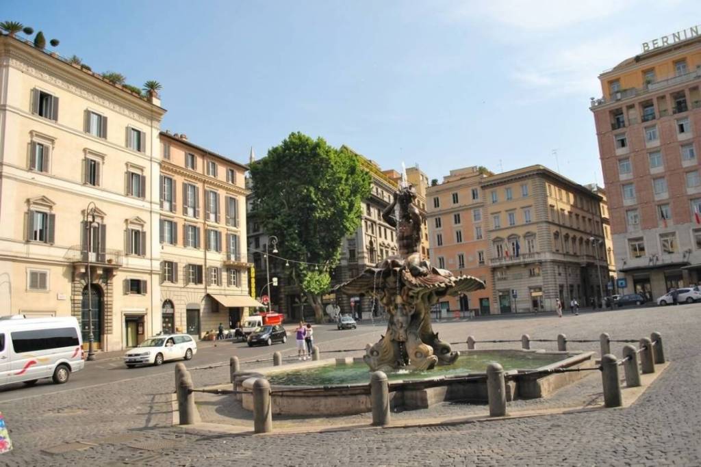 La Fontana del Tritone del Bernini al centro di Piazza Barberini a Roma, circondata da palazzi storici.