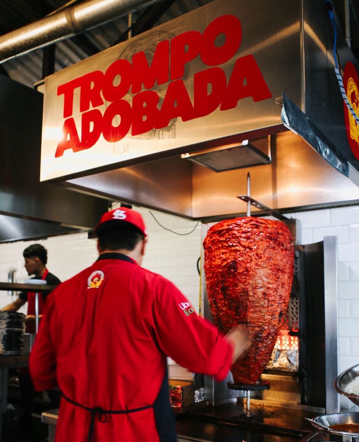 man next to adobada meat at taqueria