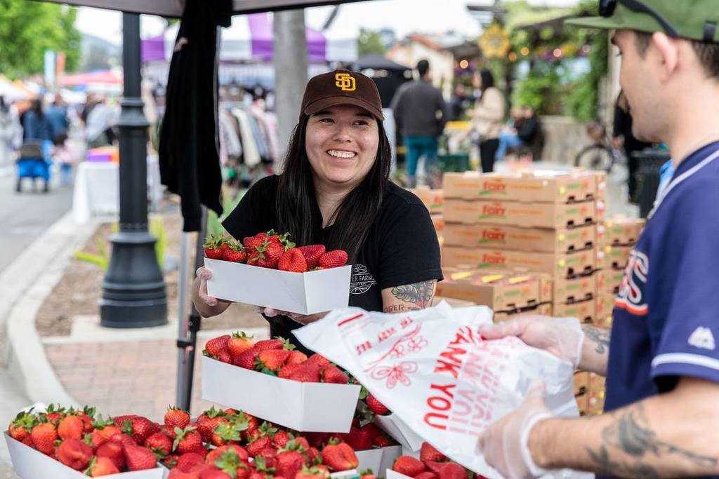 woman wearing a Padres cap selling strawberries to someone