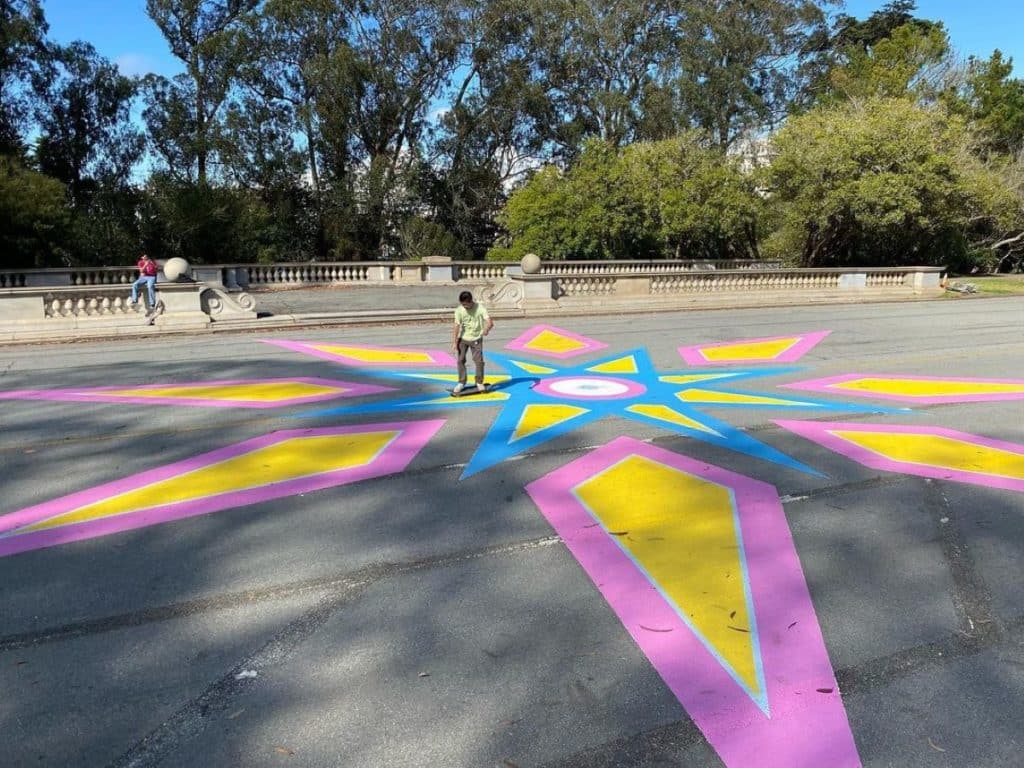 Un mural en el suelo con forma de estrella en tonos rosa, amarillo y azul en JFK Drive.