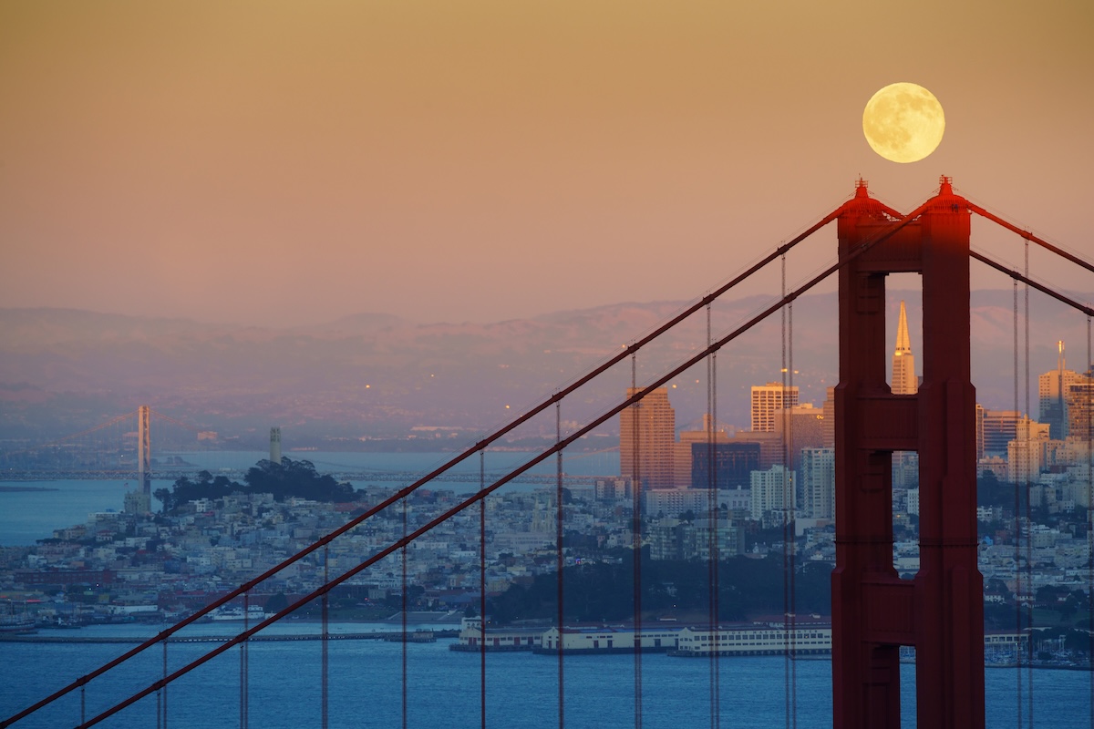 Full moon rising over Golden Gate Bridge with San Francisco urban landscape as its background