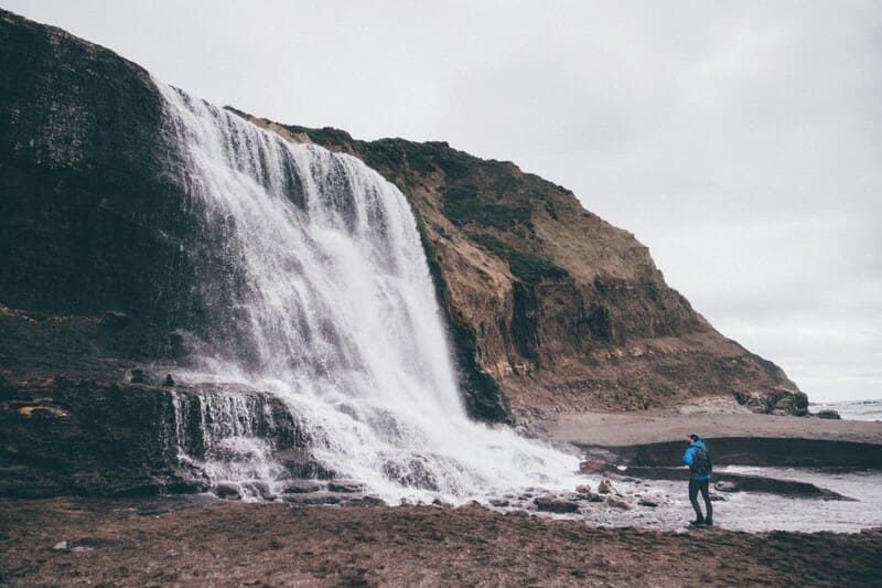 A person stands at the base of Alamere Falls on a foggy day