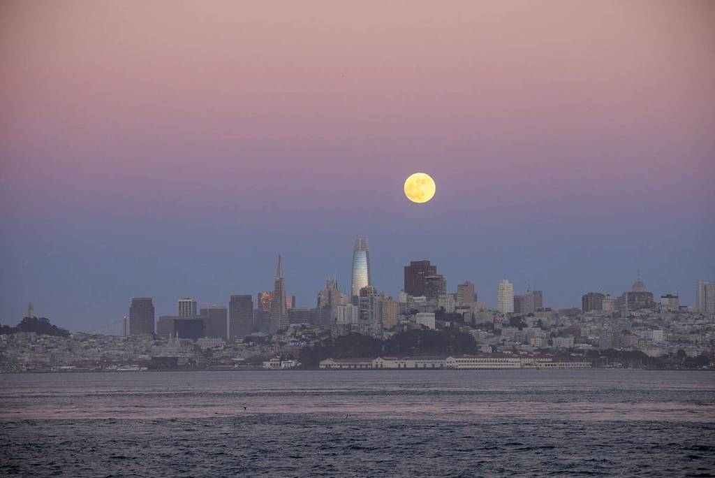 Full moon over SF skyline at sunset.