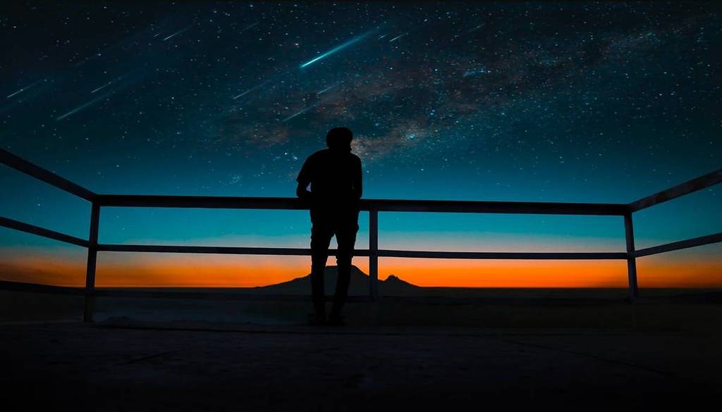 Silueta de una persona observando una lluvia de meteoritos al atardecer.