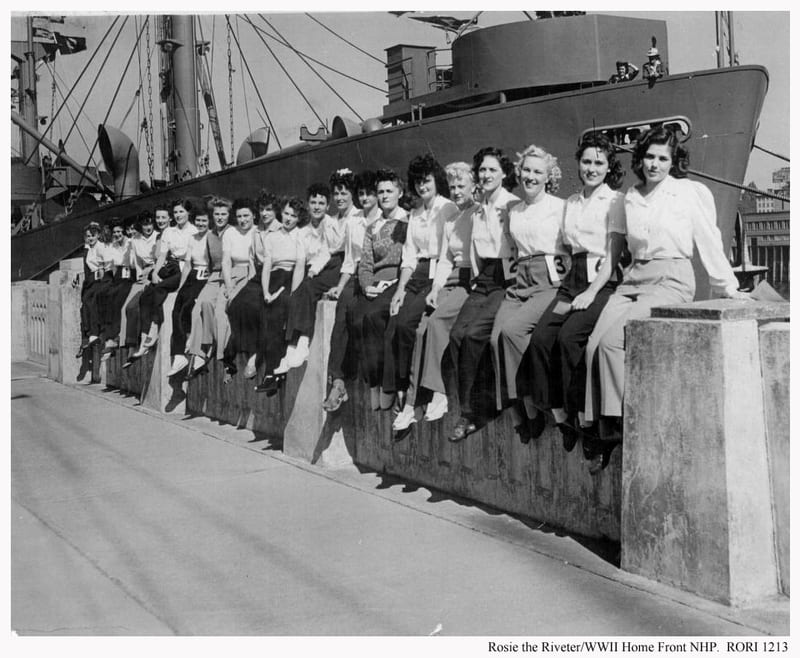 A row of women workers sit on a wall in front of a ship in Richmond.