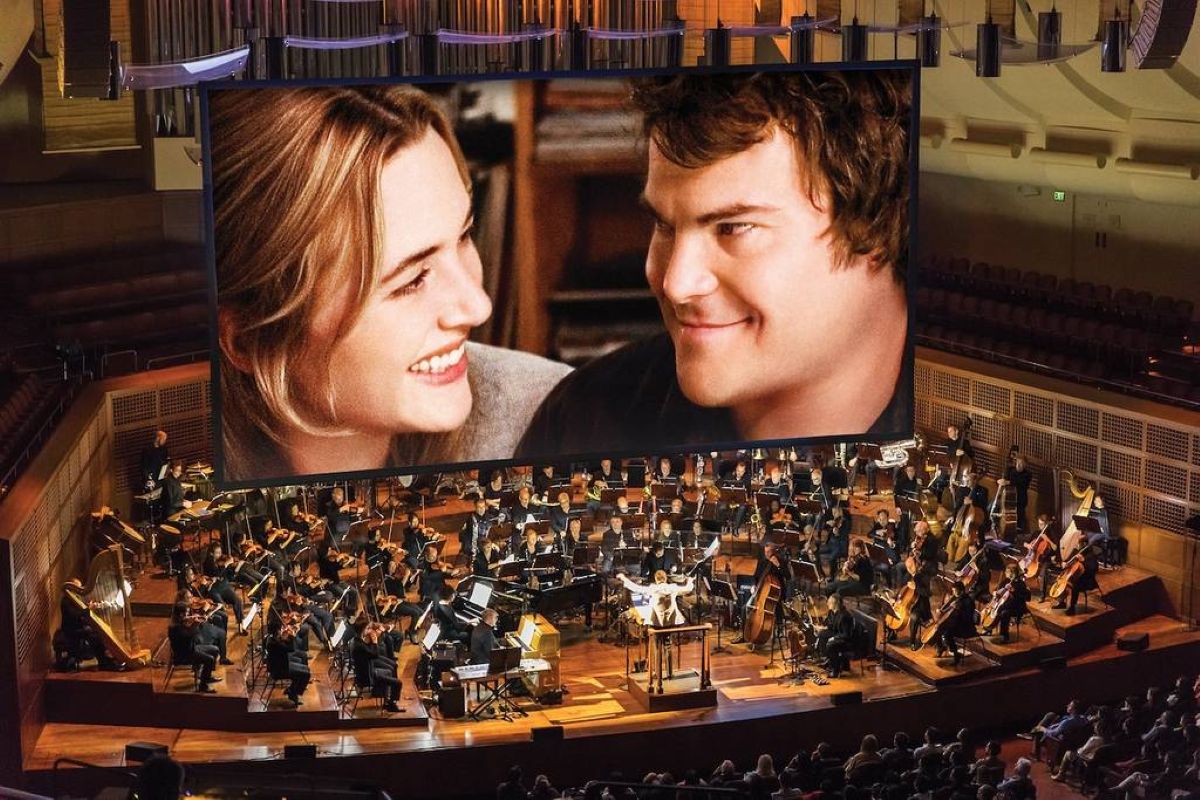 large screen shows still from movie the holiday with orchestra sat below