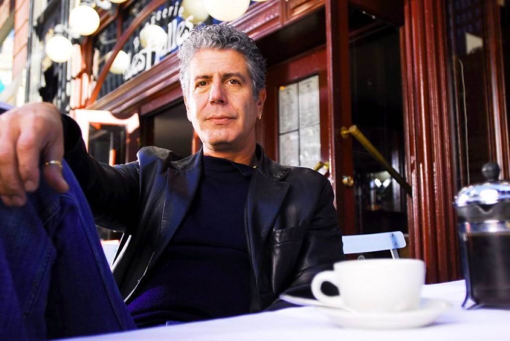 Anthony Bourdain está sentado frente a una cafetería con un café delante de él
