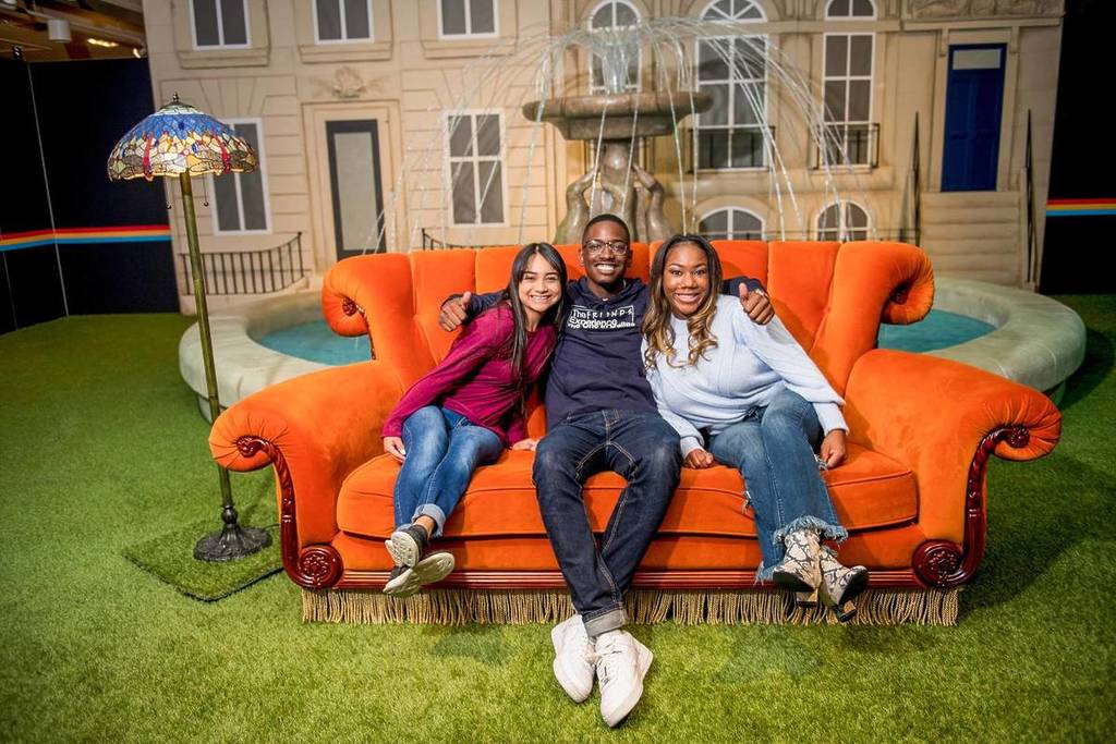 A group of visitors sat on the iconic orange couch in front of the fountain where the opening credits of FRIENDS™ takes place Singapore women's day