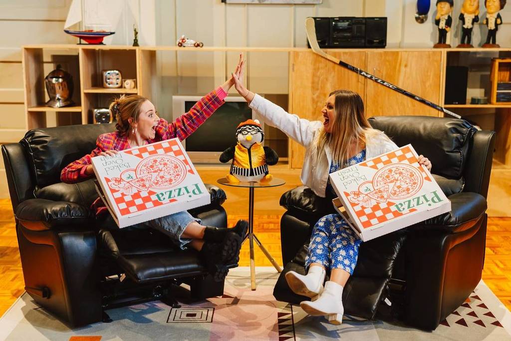 Two women high-fiving sat in Joey and Chandler's living room recliners at The FRIENDS Experience - The One In Singapore