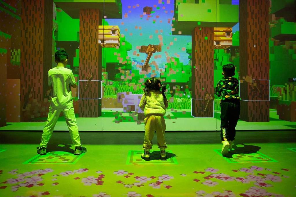 Three children chopping down virtual Minecraft trees to gather resources