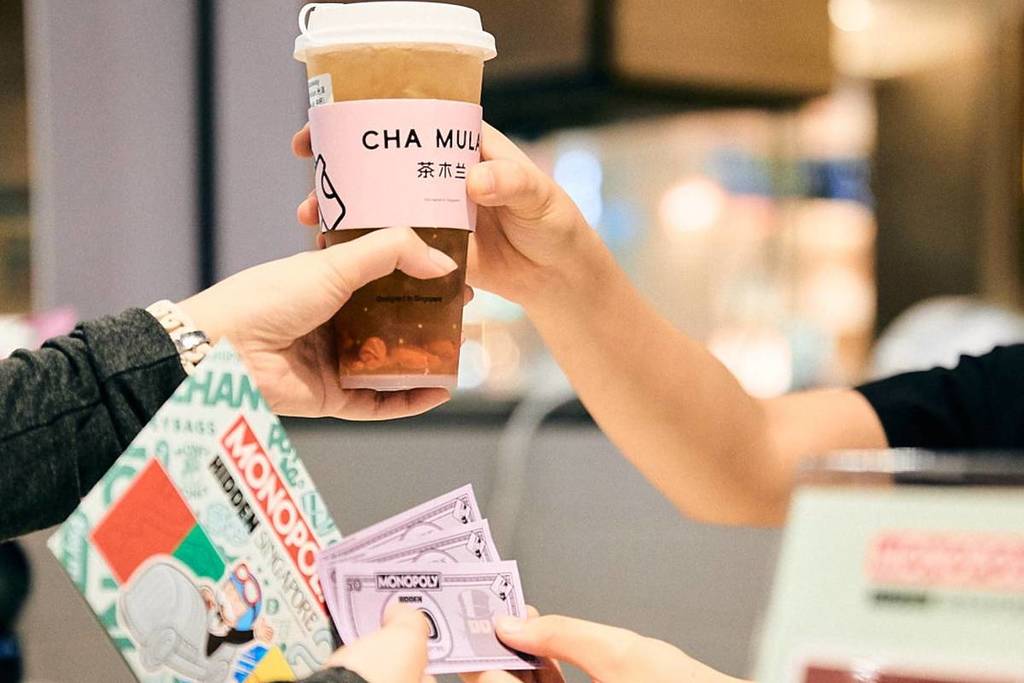 A woman exchanging MONOPOLY Money for a beverage along the MONOPOLY: HIDDEN - Changi Boulevard trail