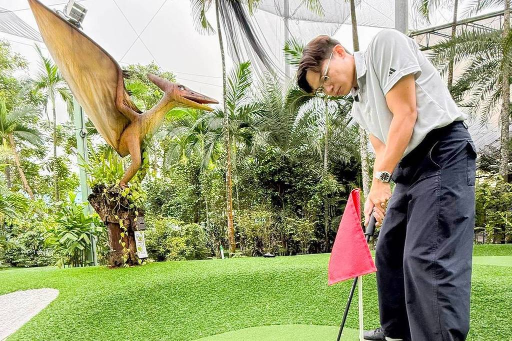A man putting a golf ball into a hole with a pterodactyl behind him at Dino Putt