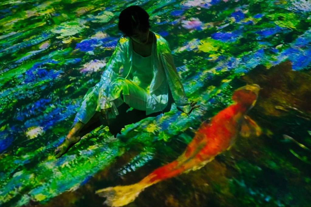 A woman sat on the floor with Monet's Koi Fish painting projected around her