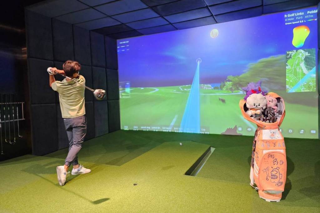 A golfer practicing his swing within the air-conditioned Indoor Simulator bay