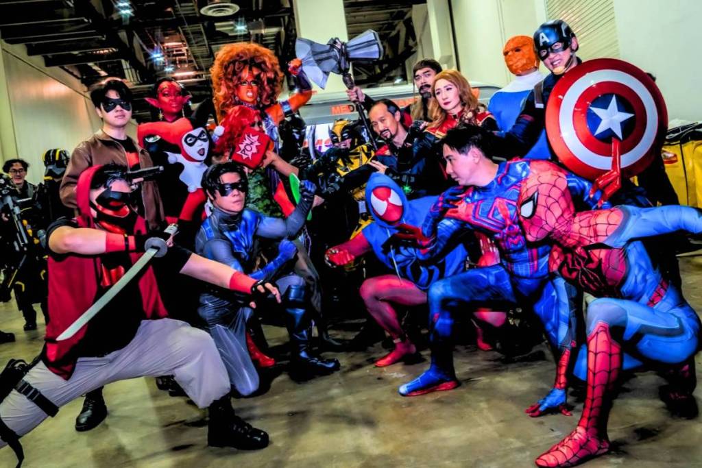 A group of cosplayers dressed up in a variety of characters such as Spider-Man, Captain America, Captain Marvel, Nightwing, Harley Quinn and more. 