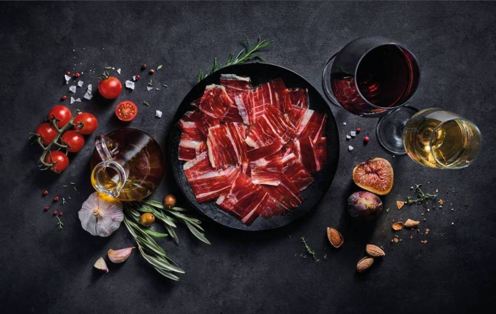 a flatlay of a plate of cured meat and glasses of wine and olive oil