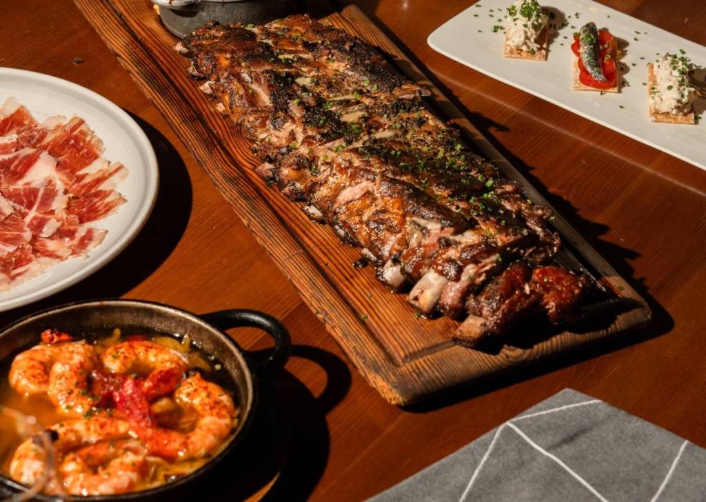 a stack of ribs, gambas and jamon on a wooden table at a spanish restaurant
