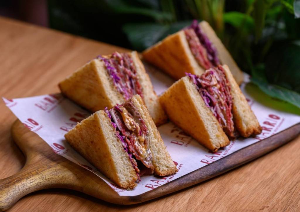 the famous "bikini" sandwich dish at barrio, the mini sandwiches are laid out on a wooden tray