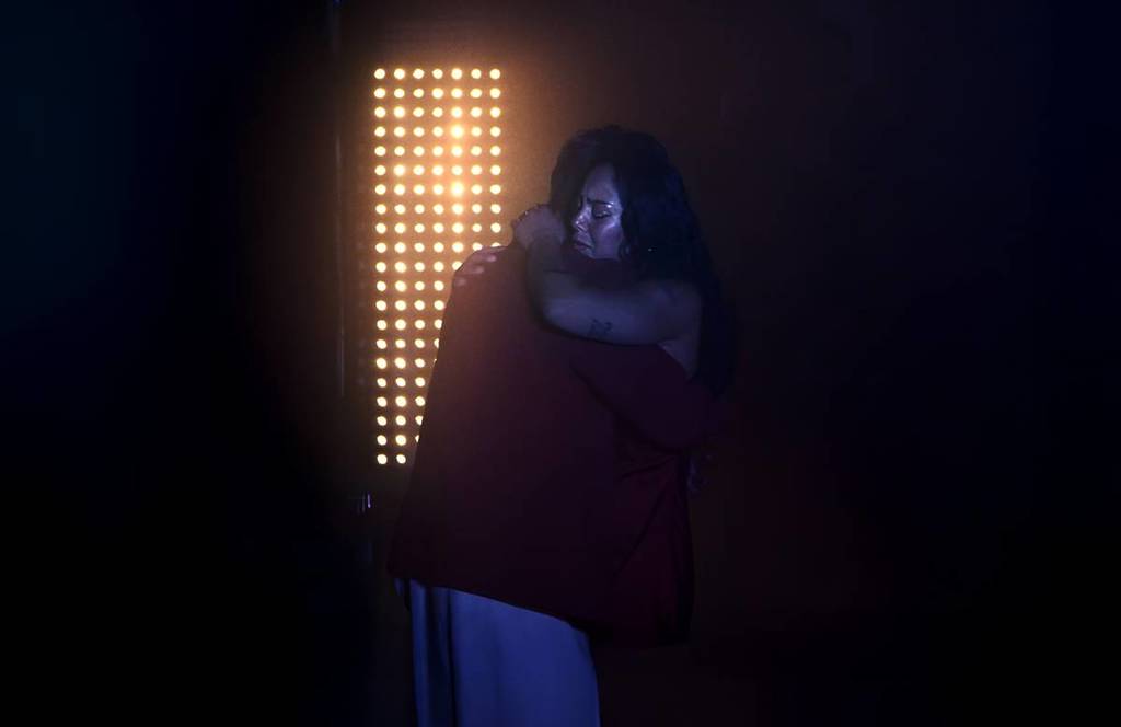 Couple of dancers hugging in the dark in front of a wall of yellow light bulbs creating emotional moment.