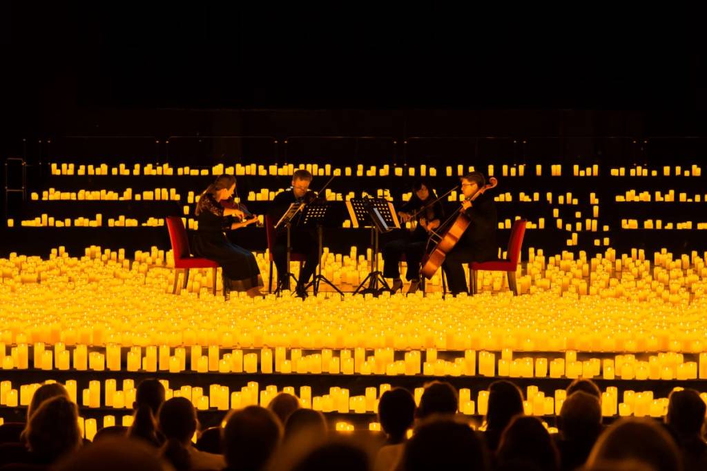 A string quartet performs on stage at a Candlelight concert, surrounded by numerous candles
