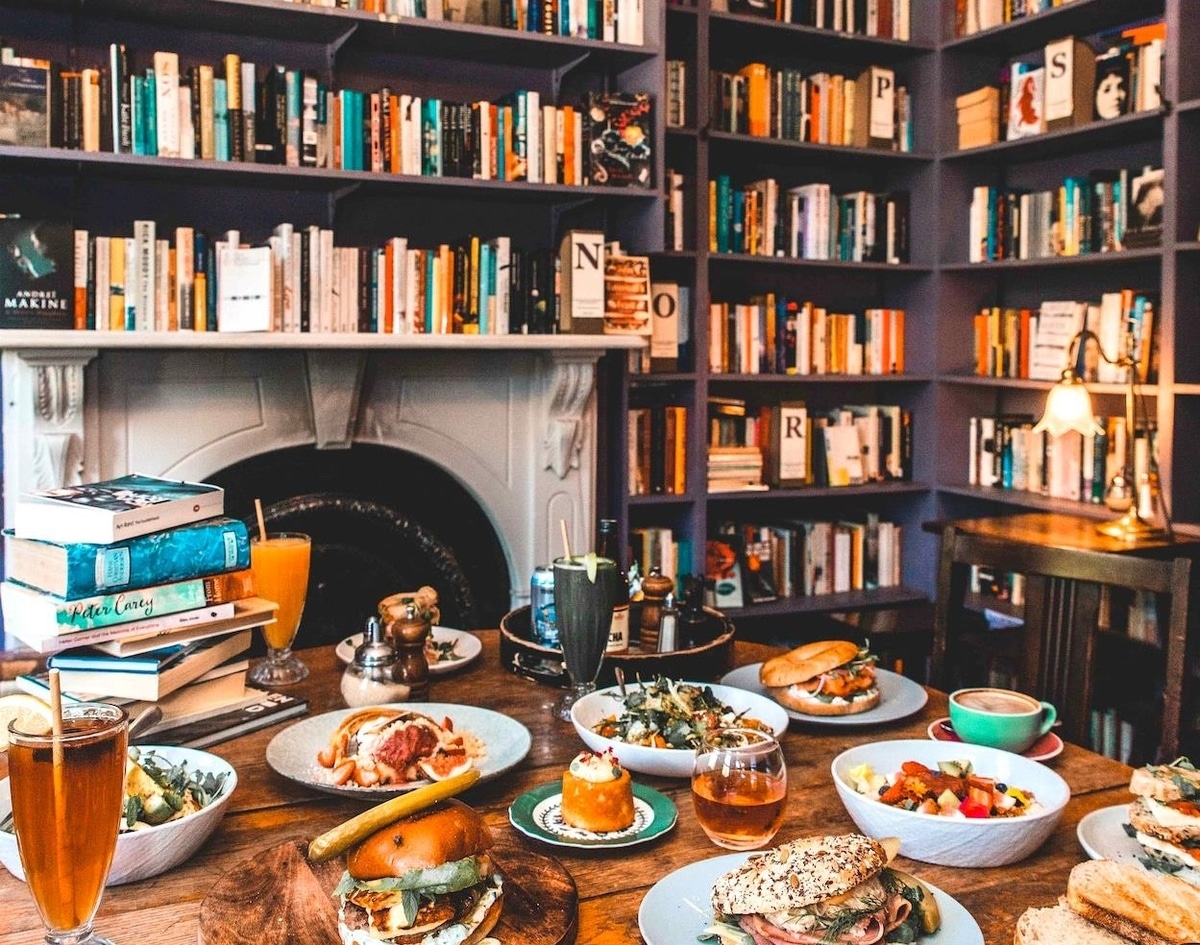 a wall lined with books alongside a table stacked with food and drink