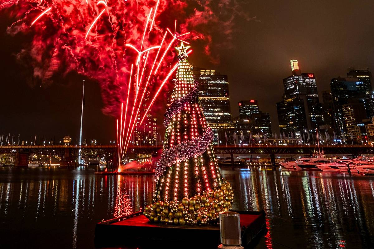 a floating Christmas tree with baubles and lights at Darling Harbour, Sydney with bright red fireworks in the background