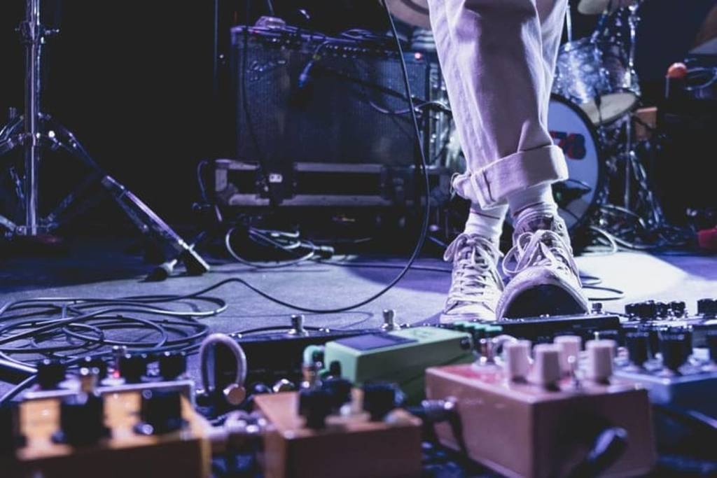 close up electric guitar pedals and someone standing on one of the pedals on stage at a live music venue