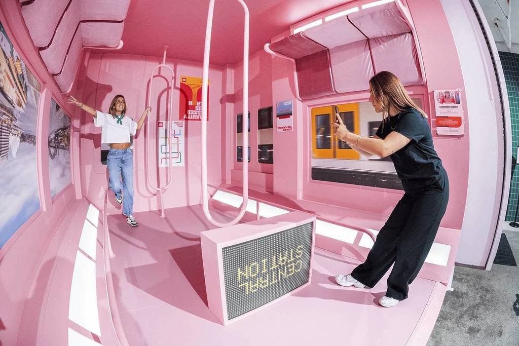 Two friends take photos in what appears to be an upside-down train at Mind Games: Art Alive!