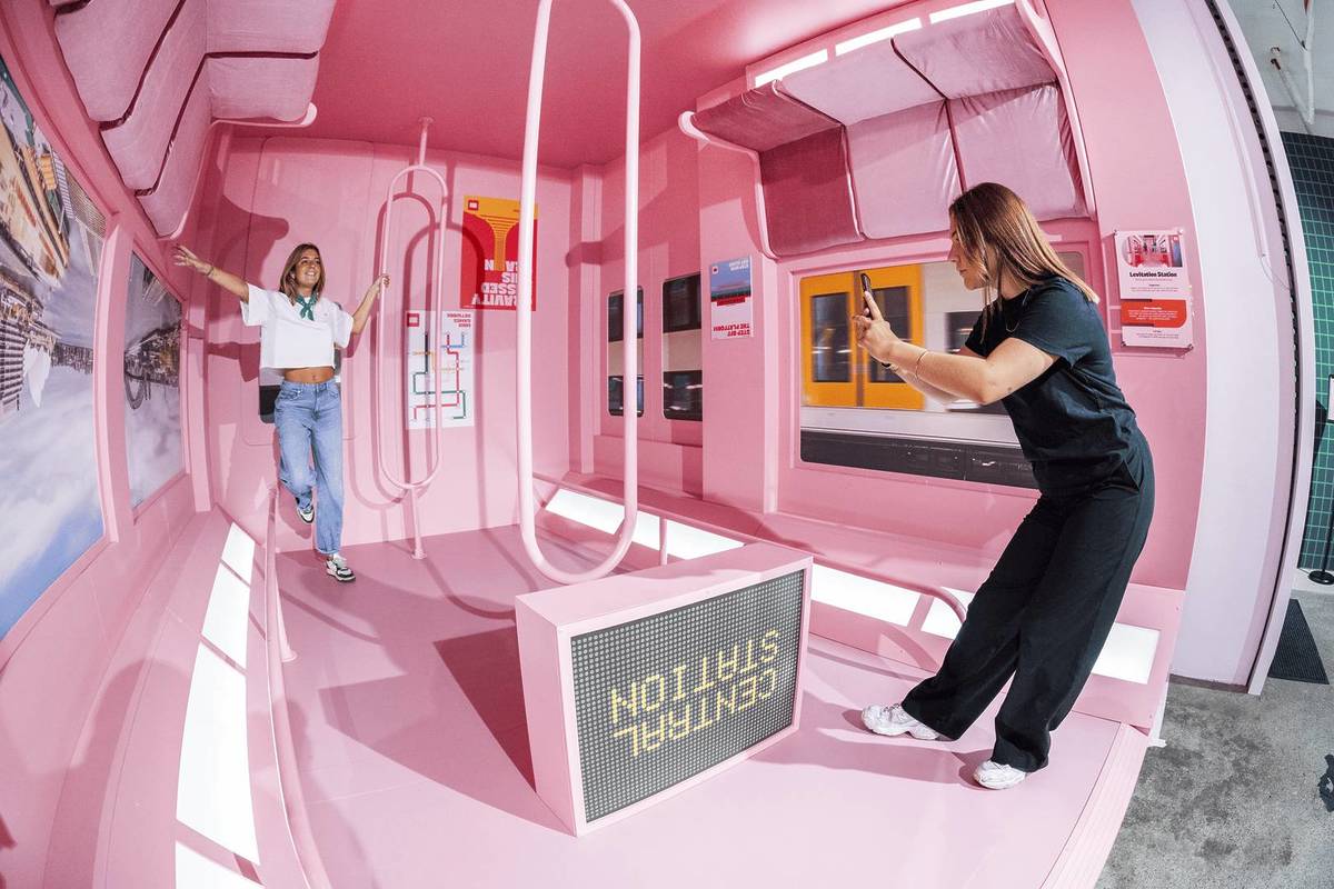 Two friends take photos in what appears to be an upside-down train at Mind Games: Art Alive!