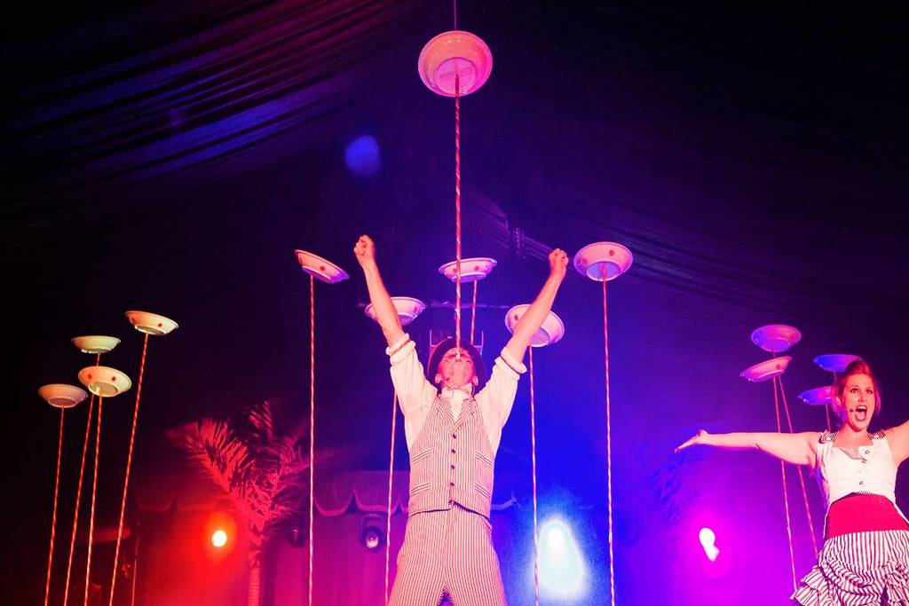 A circus performer with a stick in his mouth holding up a plate inside Sydney Spiegeltent