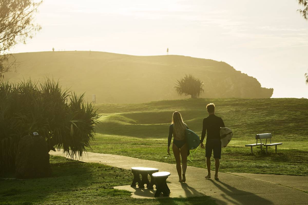 Two people walking towards the beach in Crescent Head with surfboards, sunlight streaming across the ocean