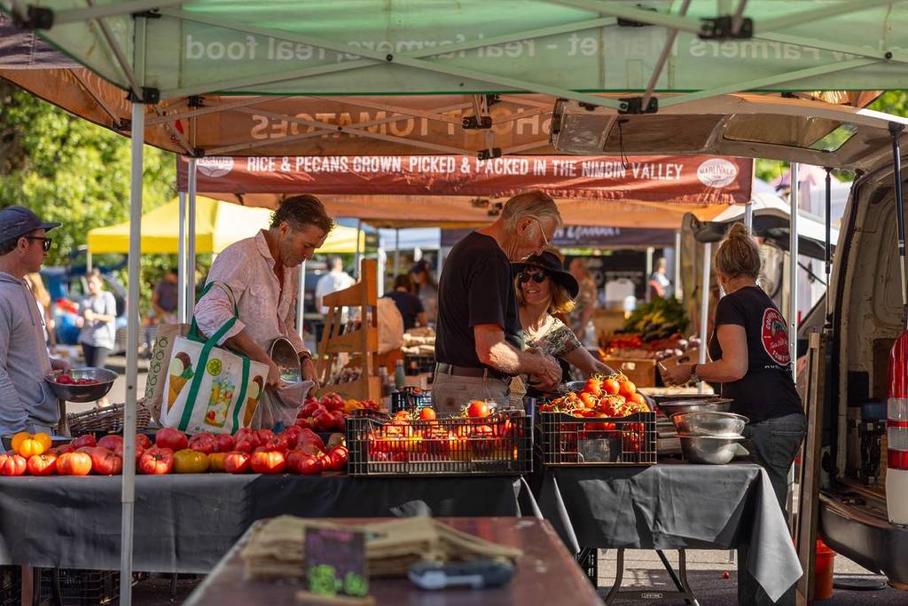 Locals and visitors buying fresh produce from fruit stalls at a vibrant market in Byron Bay