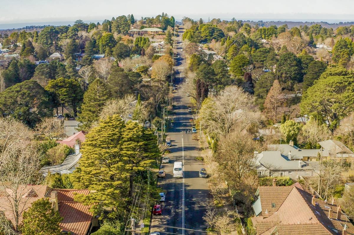 Street view of Leura with trees lining the road and the Blue Mountains visible in the distance