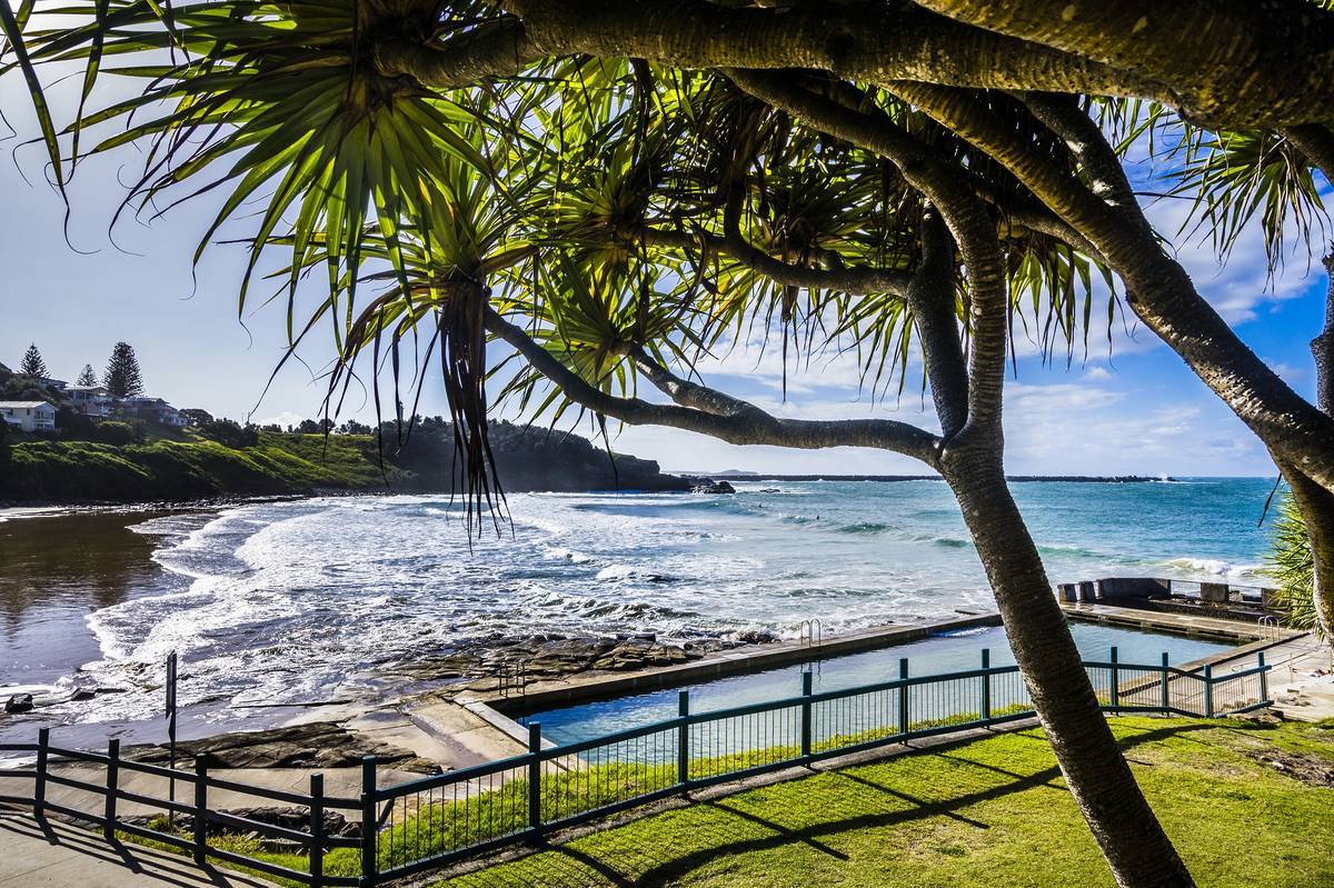 A rock pool on a Yamba beach with vibrant blue waters shimmering under bright sunshine