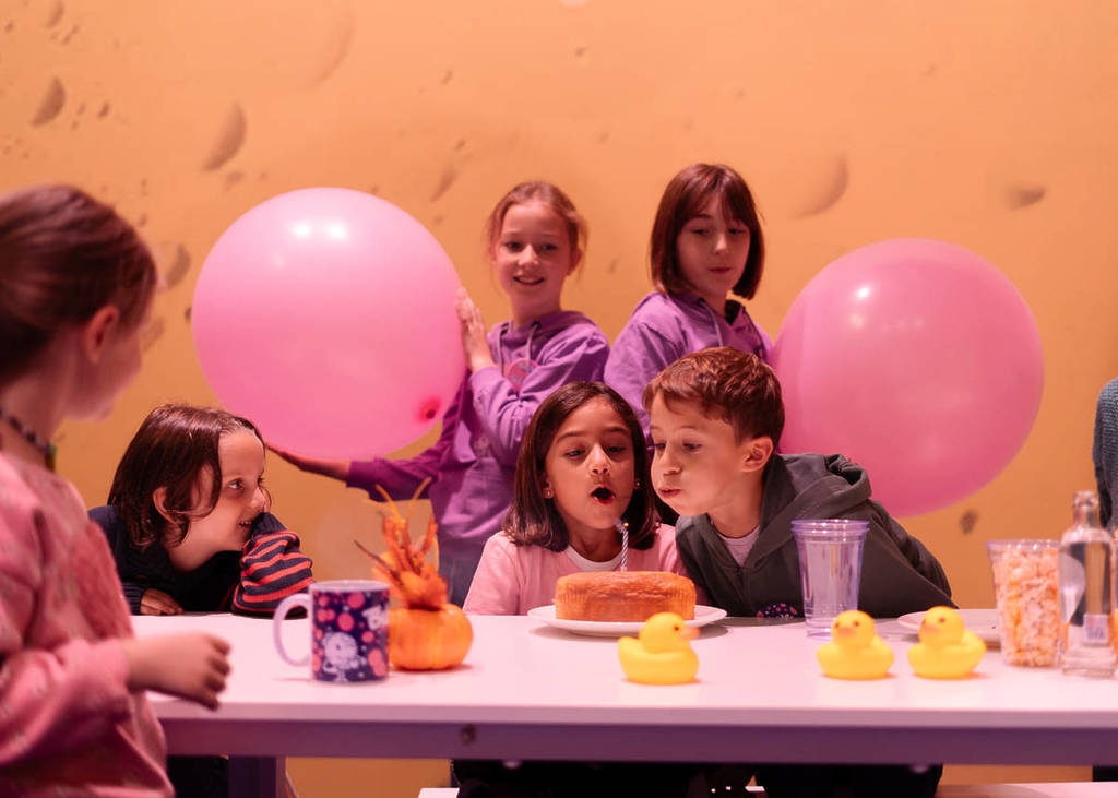 A young boy and girl blow out candles on a birthday cake at Bubble Planet.