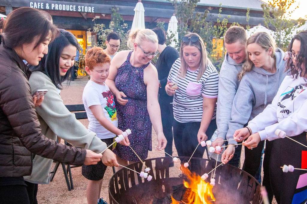 Visitors roasting marshmallows over a fire pit at Mayfield Garden in Oberon during winter