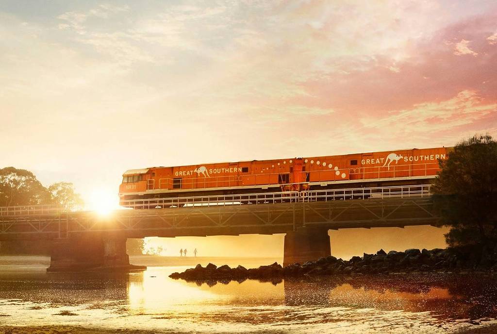 The Great Southern train crossing a bridge at sunrise, with golden light reflecting off the water