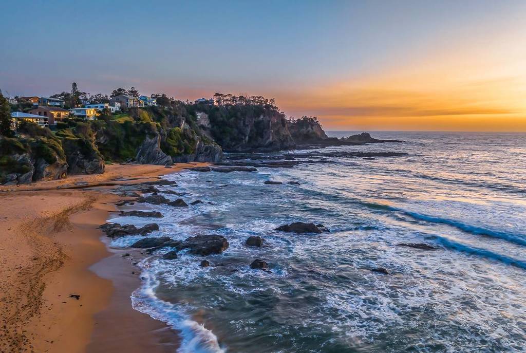 Sunrise over Malua Bay on the NSW South Coast along the Munjip Trail, with waves rolling onto a sandy beach framed by rocky headlands and coastal homes