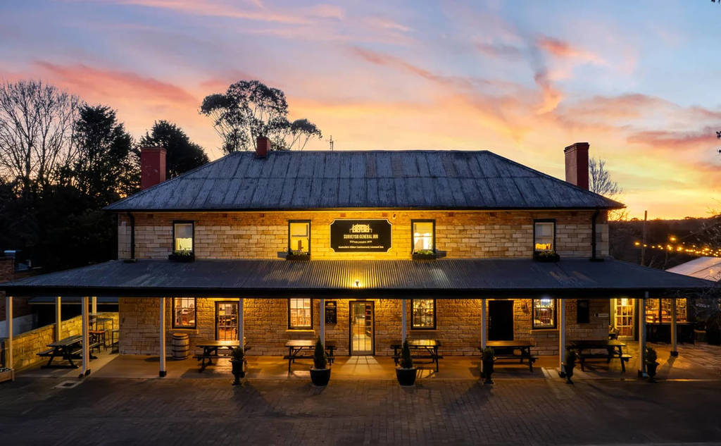 The Surveyor General Inn in Berrima at sunset, with warm lights glowing against its historic sandstone exterior