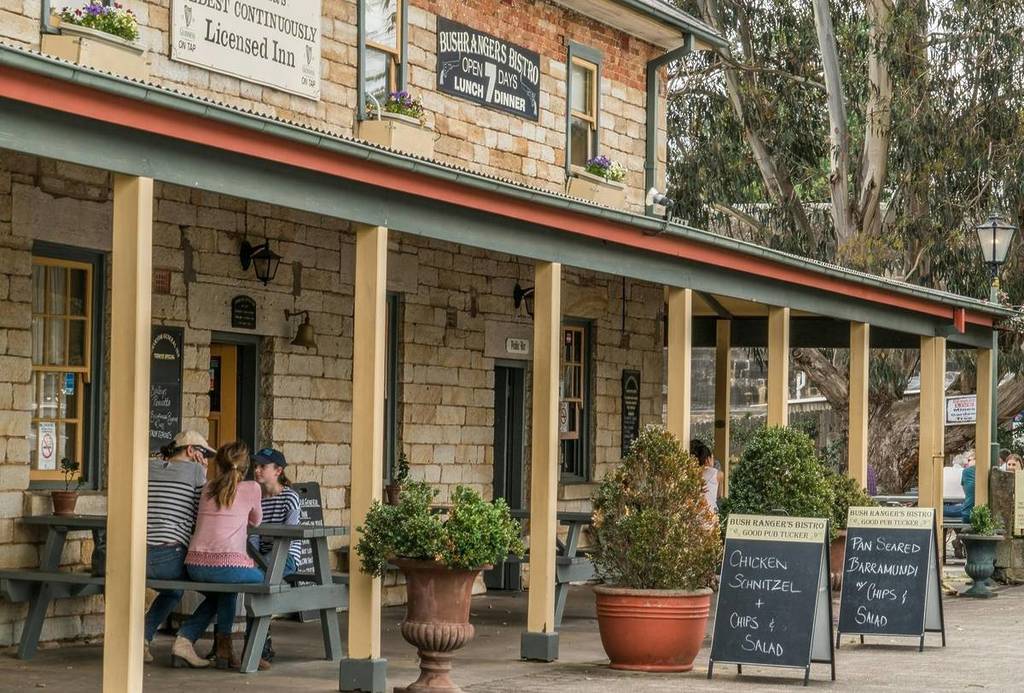The front verandah of the Surveyor General Inn in Berrima, with diners seated at outdoor tables and chalkboard signs advertising daily special