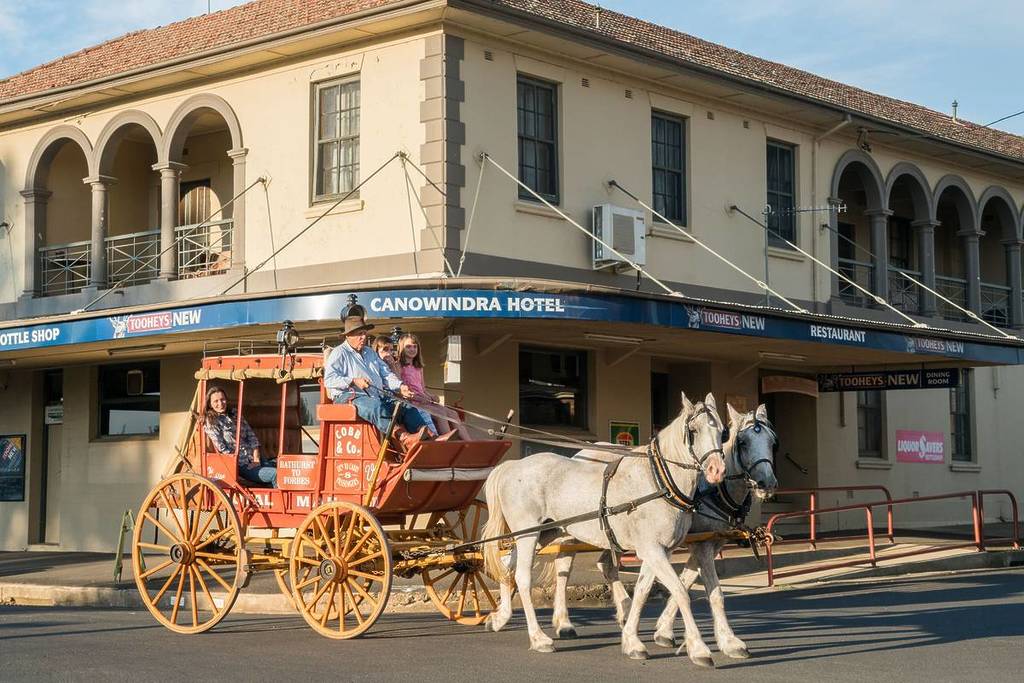 A mother and daughters enjoying a horse-drawn carriage ride through the historic streets of Canowindra, passing by the Canowindra Hotel